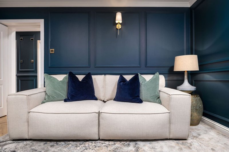 Modern living room with cream upholstered sofa, navy and green cushions, dark blue panelled walls