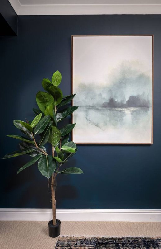Dark blue bedroom wall with potted plant and framed landscape artwork above carpet