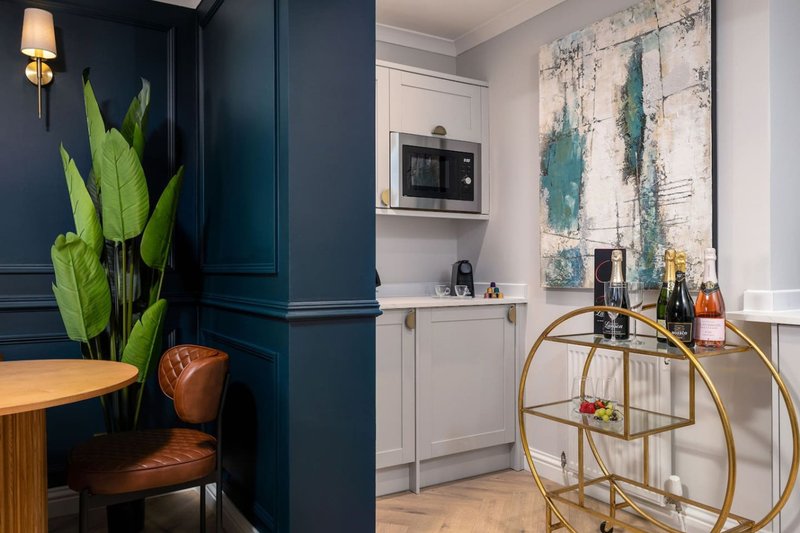 Modern kitchen with dark blue cabinetry, white counters, potted plant, and gold bar cart