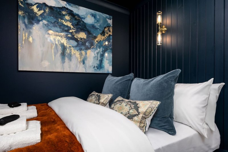 Modern bedroom with white bed, blue pillows, abstract wall art, and gold wall sconces