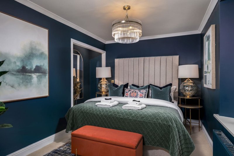 Modern bedroom with dark blue walls, upholstered headboard, green bedding, and crystal pendant light