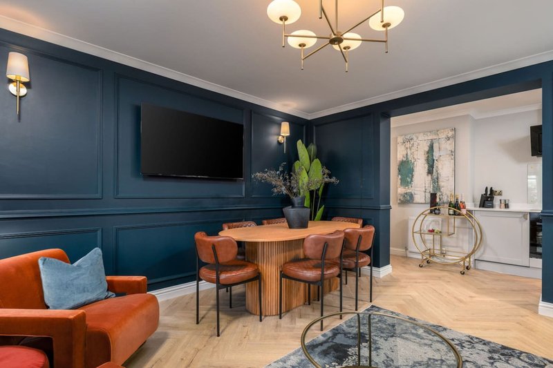 Modern living room with blue walls, orange seating, dining table, and kitchen area visible