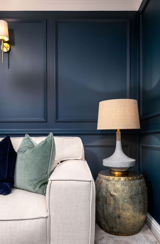 Modern living room with cream sofa, green cushion, table lamp, and dark paneled walls