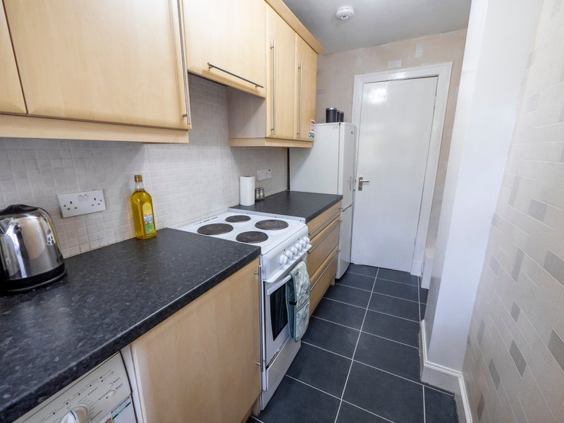 Compact kitchen with light wood cabinets, black countertops, electric cooker and dark tile flooring