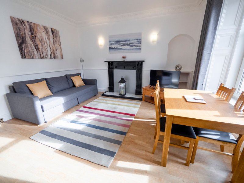 Bright living room with gray sofa, fireplace, striped rug, and wooden dining table