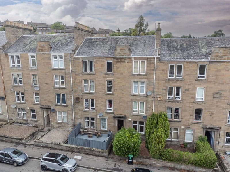 Exterior view of traditional stone tenement buildings with parked cars and street trees visible