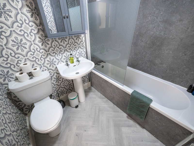 Modern bathroom with toilet, pedestal sink, bathtub, patterned tile wall and gray floor
