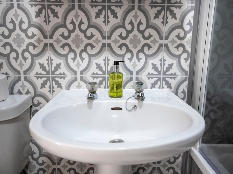 Modern bathroom with pedestal sink, patterned tile backsplash and soap dispenser