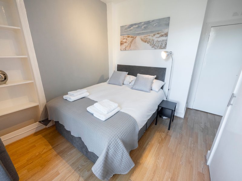 Bright bedroom with double bed, grey bedding, white towels, wooden floor and wall art