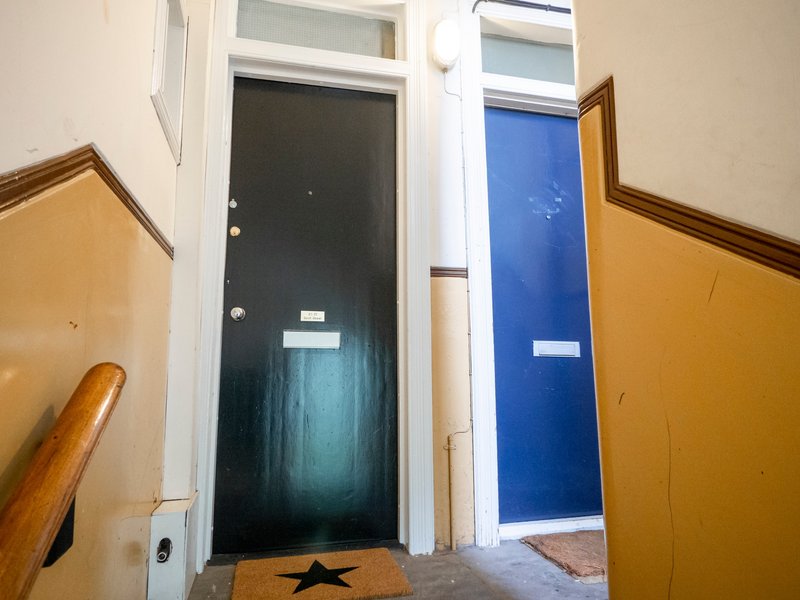 Hallway entrance with black and blue doors, wooden handrails, and welcome mat