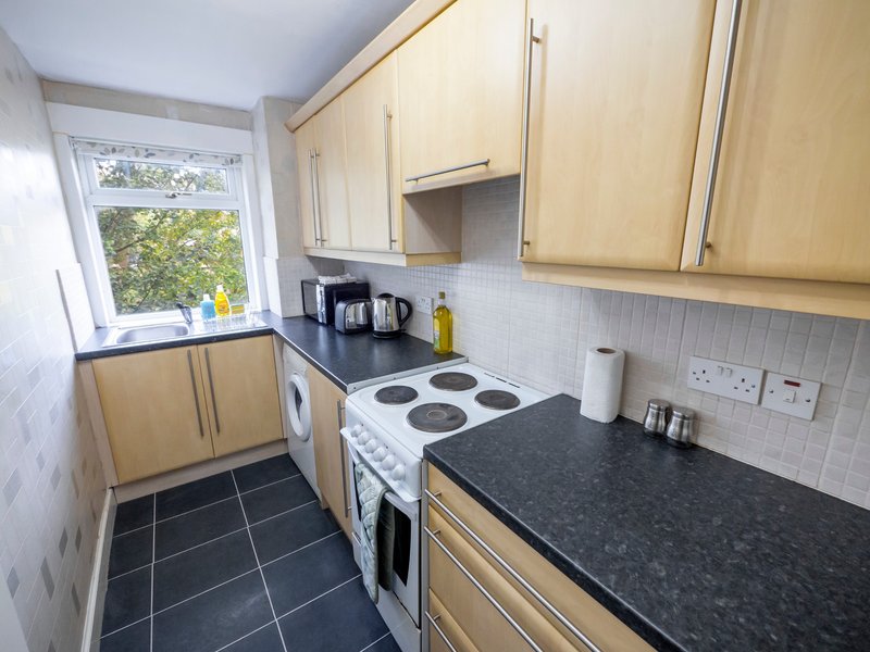 Compact kitchen with light wood cabinets, black countertops, white cooker and window