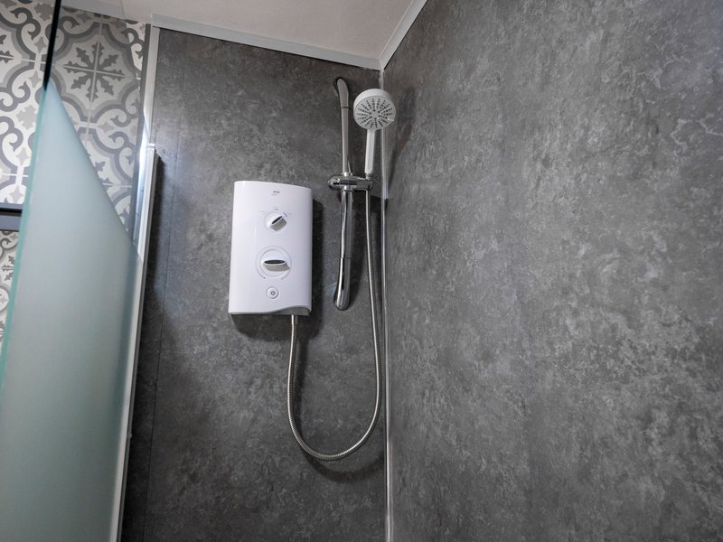 Bathroom shower area with electric shower unit and handheld showerhead