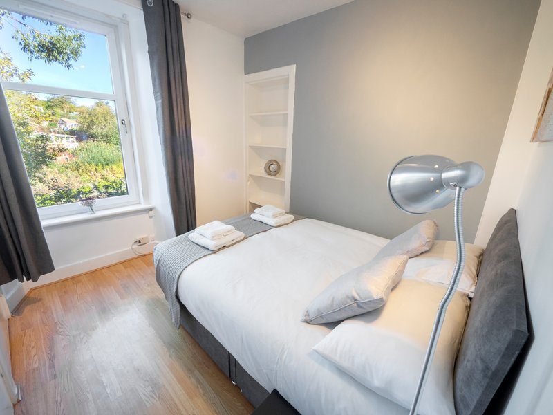 Bedroom with double bed, wooden floor, window with view, and modern wall lamp