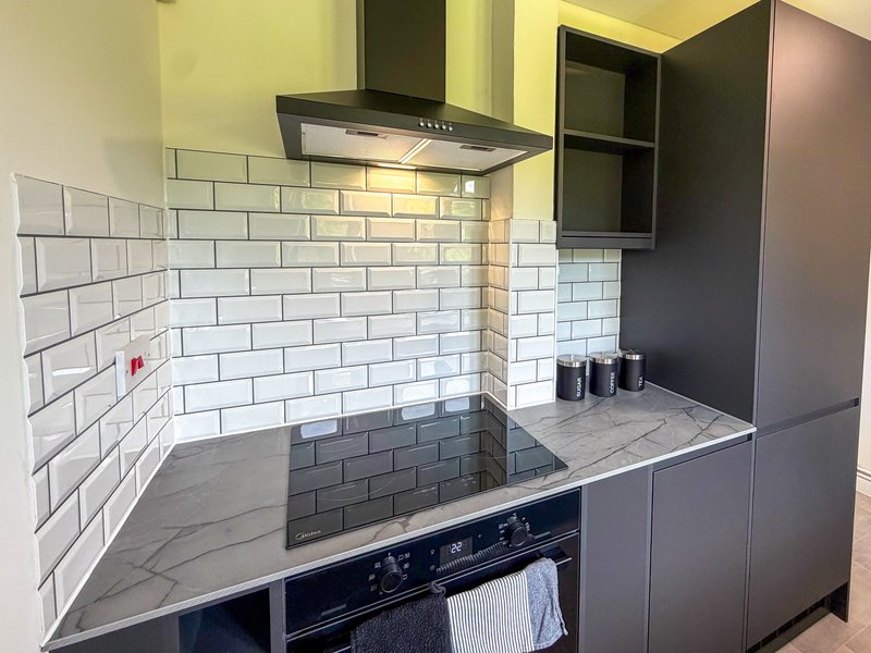 Modern kitchen with white subway tile backsplash, black cooker hood, dark cabinetry and marble-effect countertop