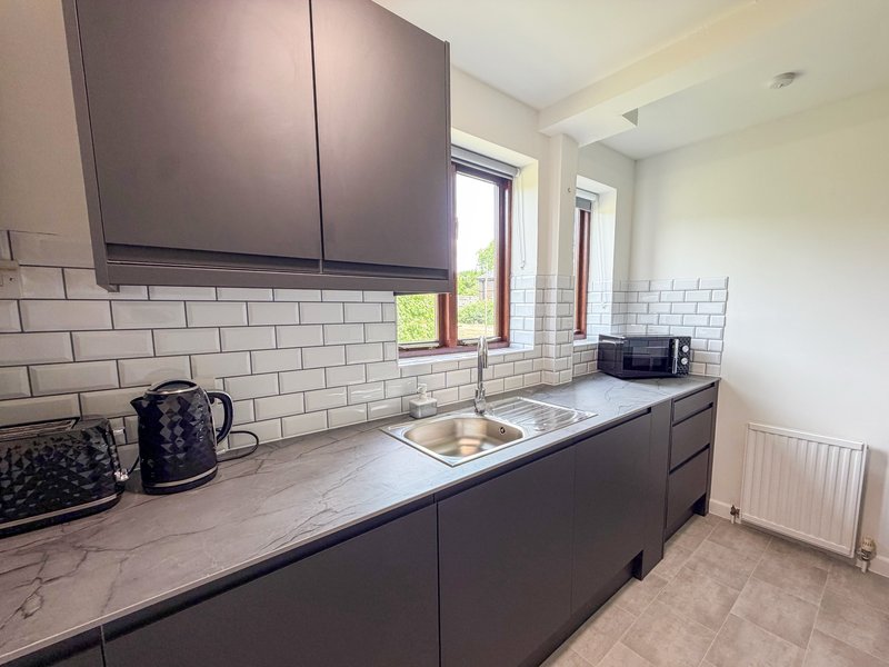 Modern kitchen with dark cabinetry, white subway tile backsplash, marble countertop and sink