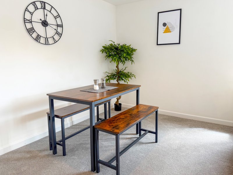 Dining area with wooden table, benches, potted plant, wall clock and framed artwork
