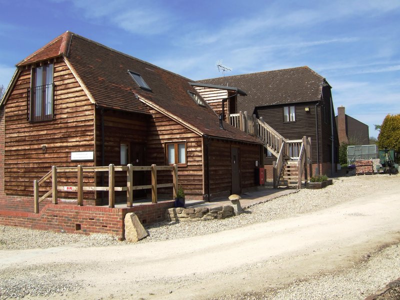 Converted barn accommodation with wooden cladding, brick base, gravel driveway and clear sky