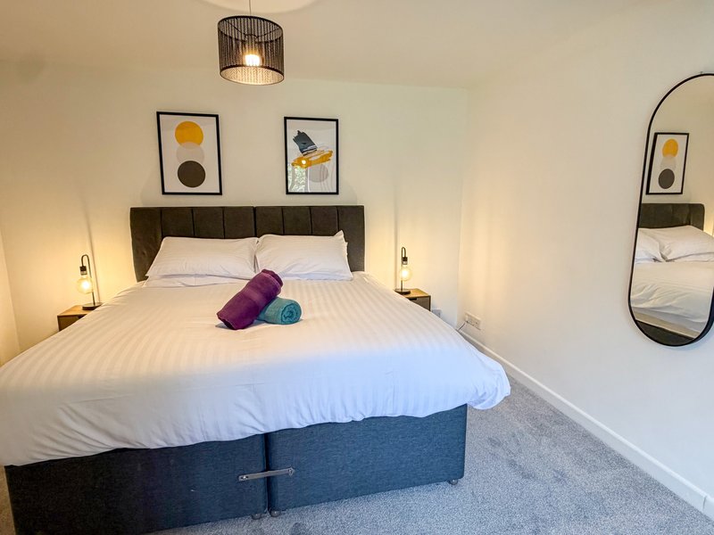 Modern bedroom with double bed, purple and teal cushions, framed wall art, and pendant light