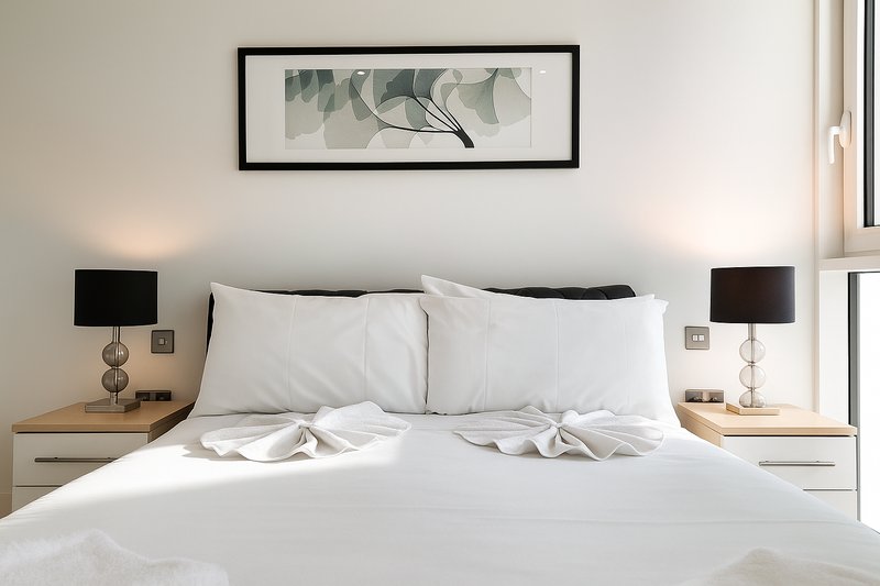 Modern bedroom with white bedding, wooden nightstands, black lamps, and framed wall art
