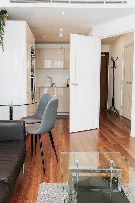 Modern open-plan living area with kitchen, dining chair, wooden flooring and glass table