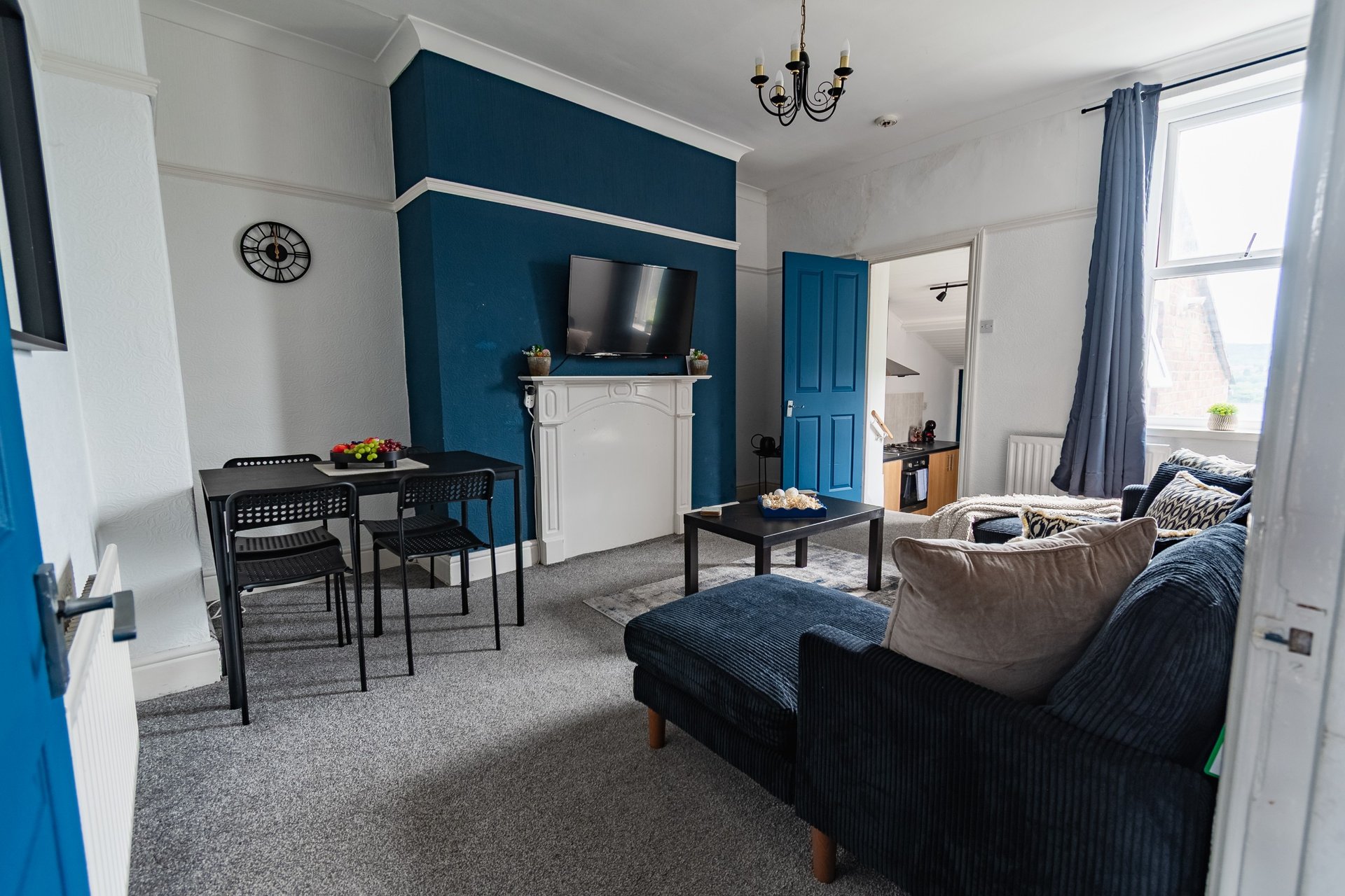 Open-plan living area with navy feature wall, fireplace, dining table, sofa and armchair