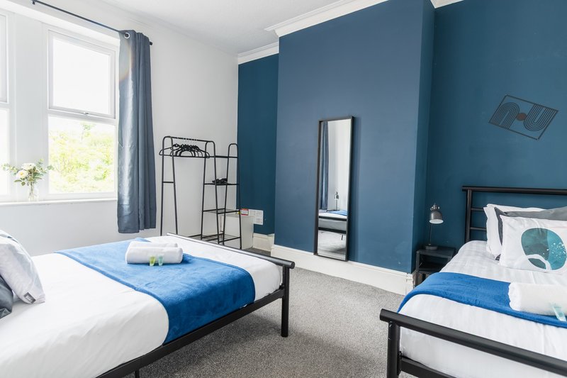 Bright twin bedroom with blue accent wall, white bedding, and modern furnishings