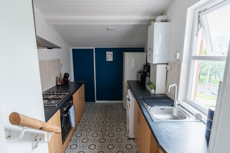 Galley kitchen with wooden cabinets, gas stove, sink, and blue wall paneling