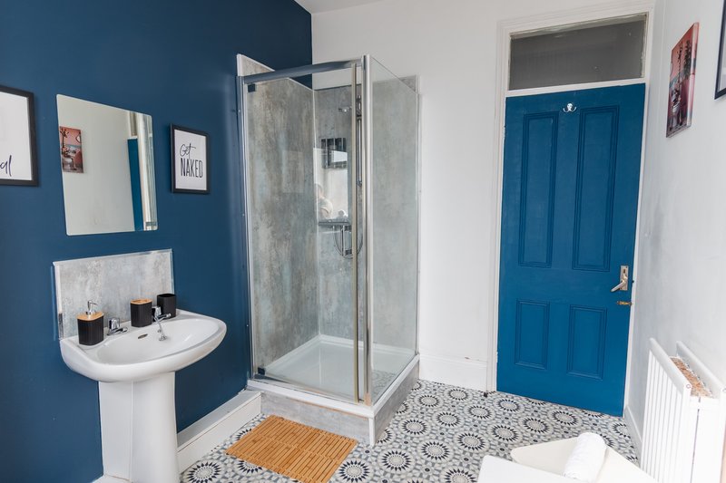 Modern bathroom with pedestal sink, shower enclosure, blue walls and patterned floor tiles