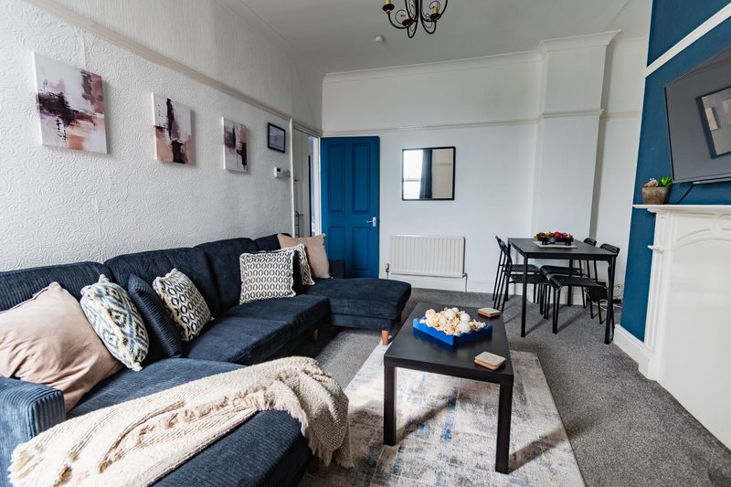Open-plan living room with navy corner sofa, black coffee table, dining area and blue accent wall