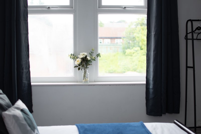 Bedroom with double bed, large window with black curtains and flower vase on sill