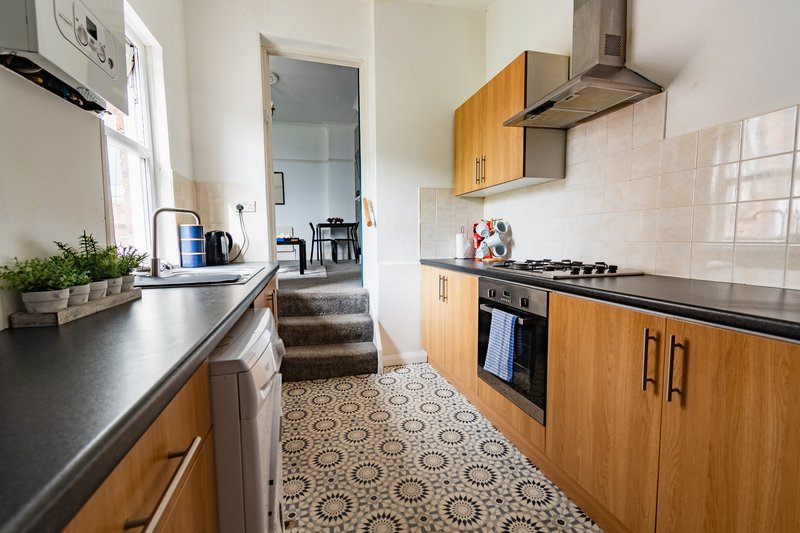 Galley kitchen with wooden cabinets, black countertops, gas range, and patterned tile floor
