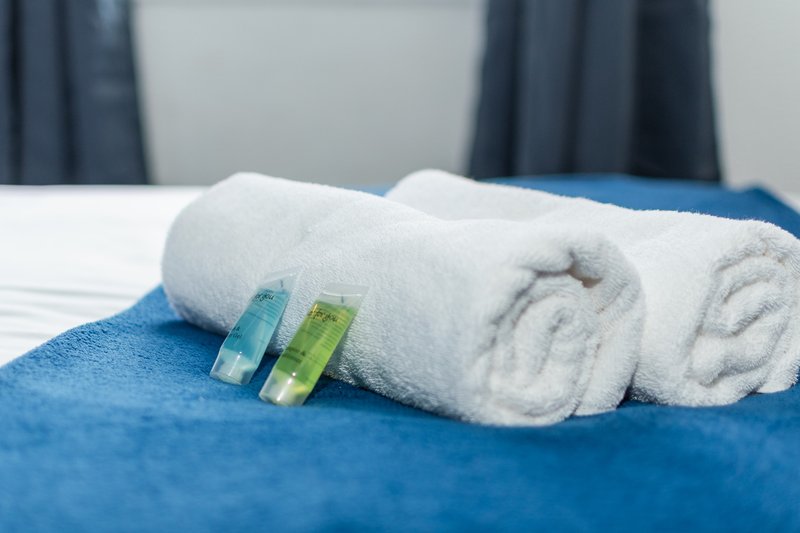 Bedroom detail with rolled white towels and toiletries on blue bedspread