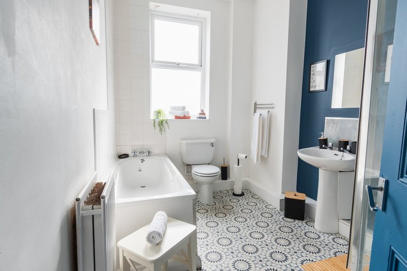 Bright bathroom with white bathtub, toilet, sink, patterned floor tiles and blue accent wall