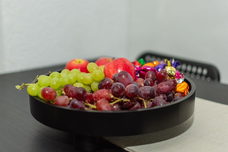 Black bowl with fresh grapes, apples and edible flowers on dark table