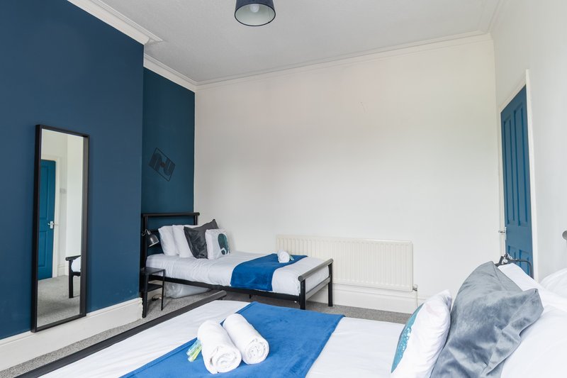 Modern bedroom with two single beds, blue and white bedding, dark blue accent wall and mirror
