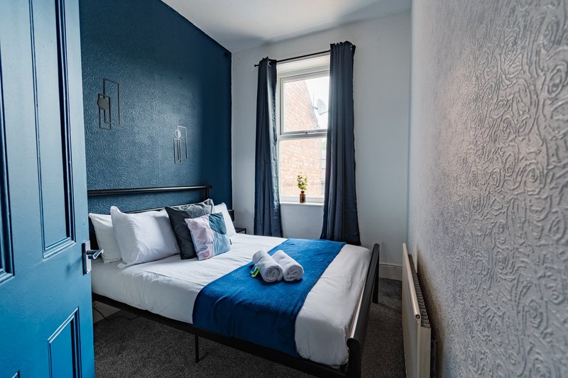 Bedroom with blue feature wall, double bed, white bedding, blue throw, and window with dark curtains