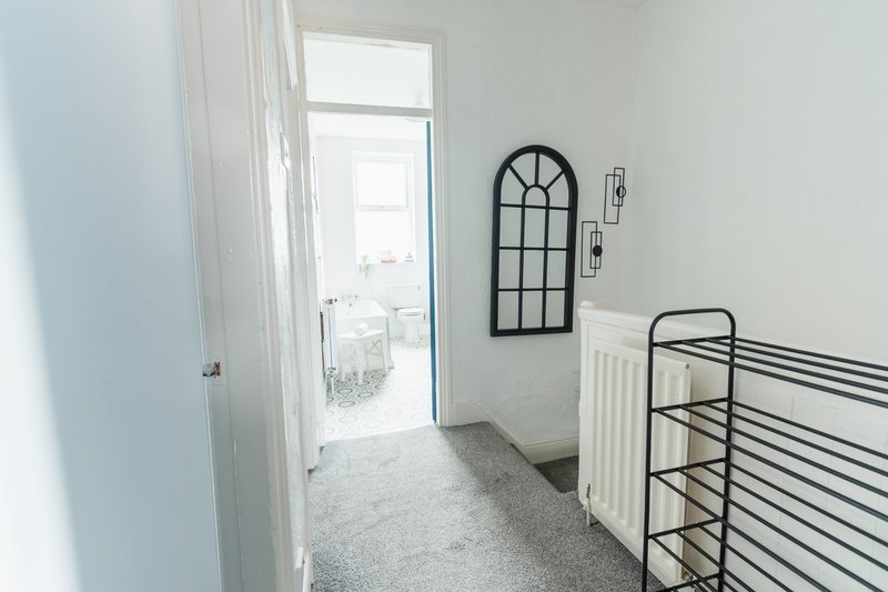 Bright hallway with white walls, metal stair railing, decorative arched mirror and door to balcony