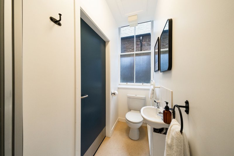 Modern bathroom with dual sink, toilet, mirror, window and dark blue door