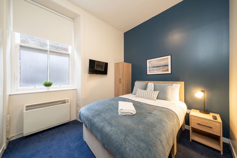 Bedroom with double bed, blue accent wall, wooden furniture, and window with radiator