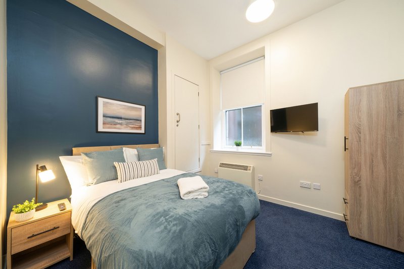 Modern bedroom with double bed, blue accent wall, wooden nightstand and wall-mounted TV