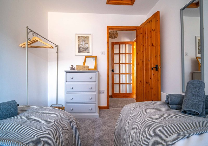 Twin bedroom with two beds, wooden wardrobe, chest of drawers, coat stand and framed wall art