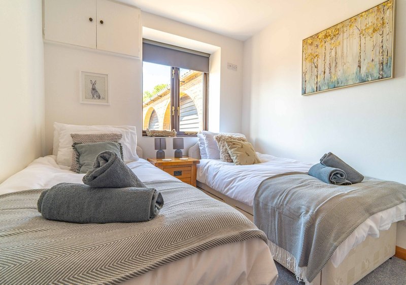 Bright bedroom with two single beds, rolled towels, window with sea view, and framed artwork