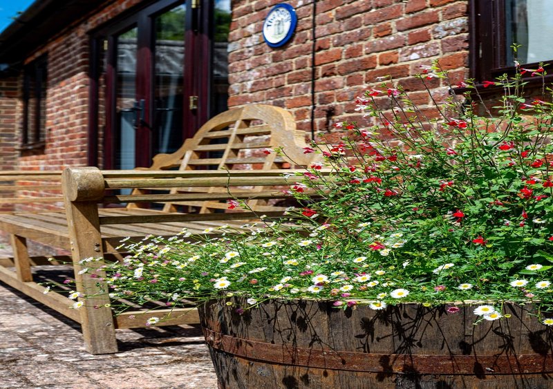 Brick property exterior with wooden bench, flowering planters, and clock on wall