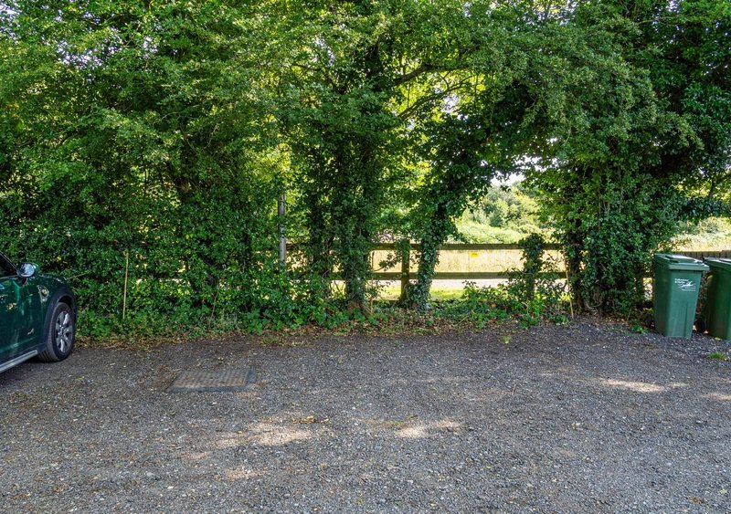 Driveway with gravel surface, ivy-covered archway, parked car and bins visible