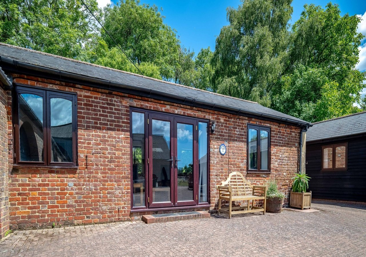 Modern brick cottage exterior with patio, featuring French doors and garden seating area