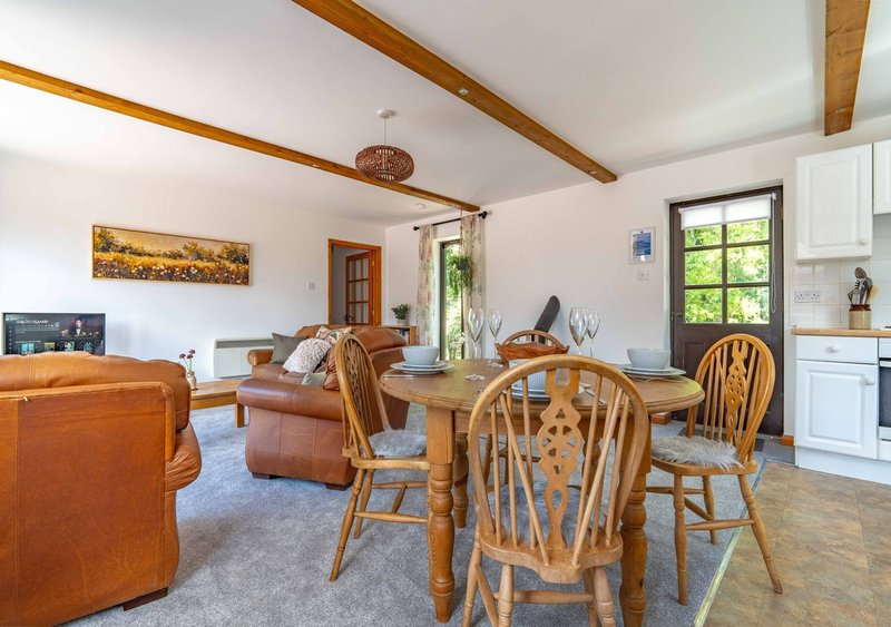 Open-plan living and dining area with wooden beams, leather furniture, dining table and chairs
