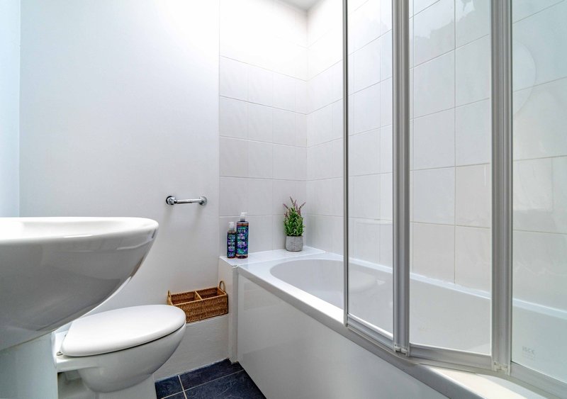 Clean modern bathroom with white toilet, shower enclosure, sink and tiled walls