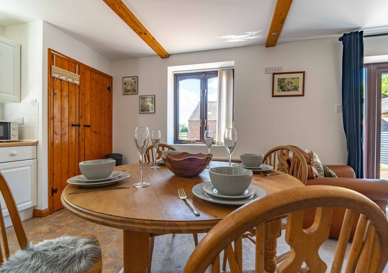 Dining room with round wooden table, place settings, wooden chairs, and open kitchen area