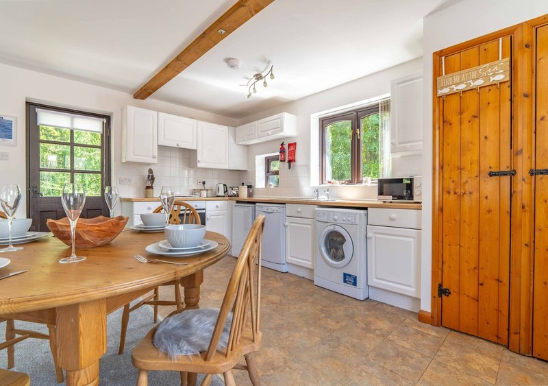 Open-plan kitchen and dining area with wooden table, white cabinetry, washing machine and wooden doors