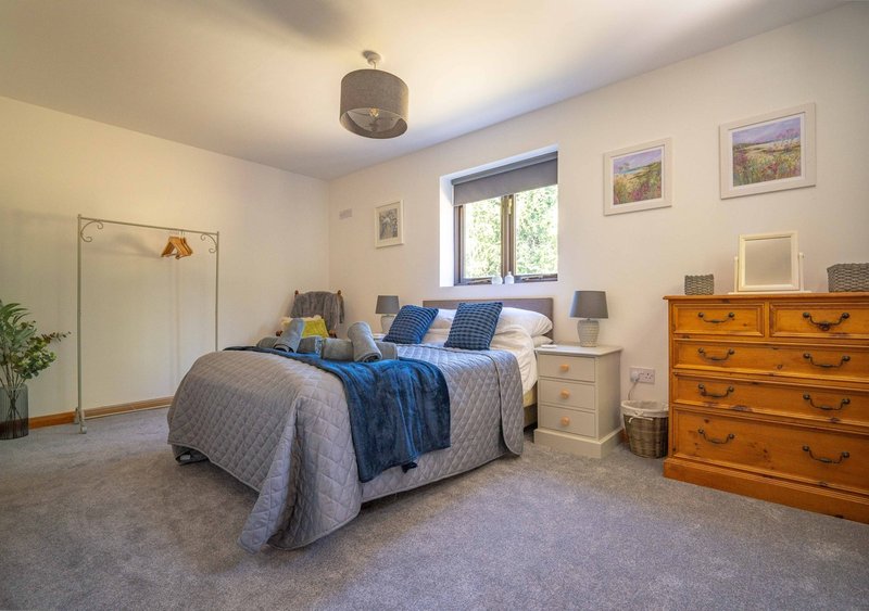Spacious bedroom with double bed, wooden dresser, bedside tables, and window with natural light